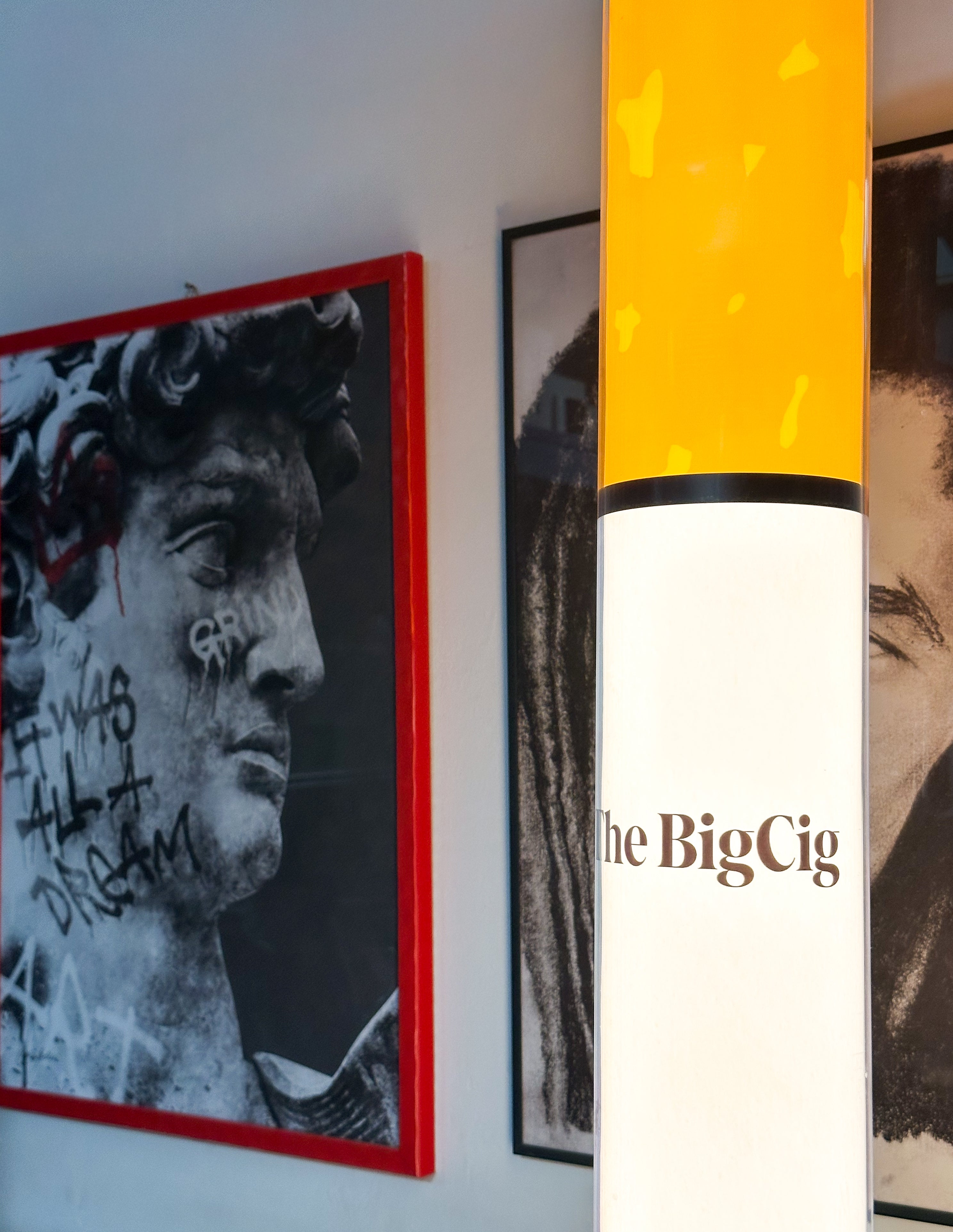 Framed artworks on a wall with 'The Big Cig' visible